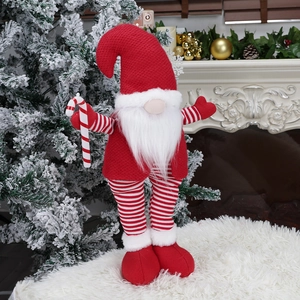Christmas gnome doll with red knitted hat and candy cane standing near fireplace