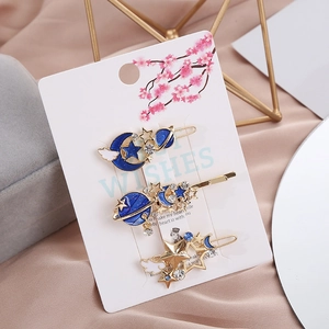 Set di tre fermagli dorati con stelle e lune blu su cartoncino a motivi floreali