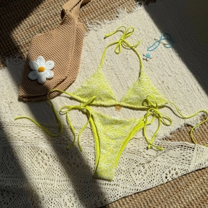Two-piece lime green bikini set with daisy print and halter neck tie on woven mat