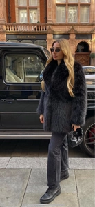 Manteau chic en fausse fourrure noire avec un sac à main tissé devant une voiture