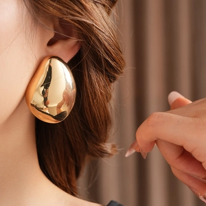 Close-up of a large irregular golden pebble earring on a female model's ear
