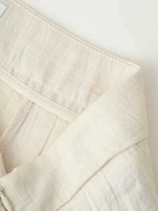 Detailed macro view of beige linen shorts waistband showing neat stitching and hidden zipper