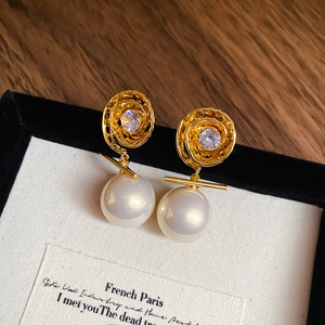 Détail de boucles d'oreilles vintage dorées avec spirale, zircon et grande perle blanche