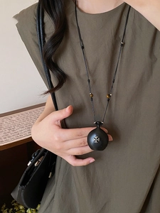 Détail du collier pendentif cœur en bois avec croix en métal sur robe vert foncé