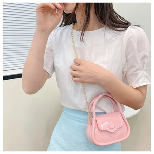 Close-up of a mini pink jelly bag with gold chain strap carried by a model
