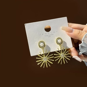 Detail of golden sunburst drop earrings with central pearl and rhinestone studs