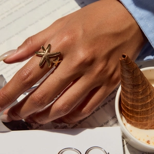 Close-up of golden starfish open ring with textured grain detail on a model's finger