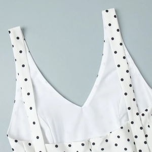 Détail de l'encolure en V et des bretelles avec motif à gros pois noirs sur fond blanc