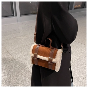 Detail of a brown suede crossbody bag with white faux fur trim and gold hardware accents