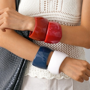 Minimalist resin geometric thick bangles in red, blue, and white worn by a model