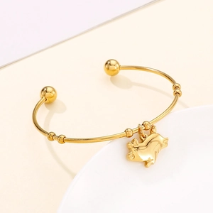 Gros plan sur un jonc doré minimaliste avec pendentif cochon sur fond crème élégant