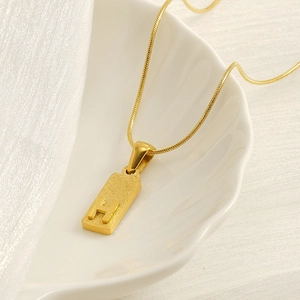 Gold stainless steel rectangle pendant necklace with textured letter H in a shell dish