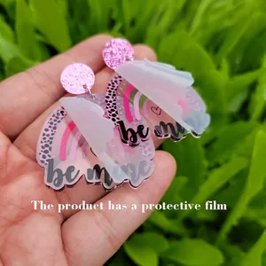 Detail of acrylic earrings with pink leopard print rainbow and 'be mine' text