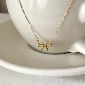 Elegant gold bow pendant necklace in 925 sterling silver hanging on a white ceramic cup