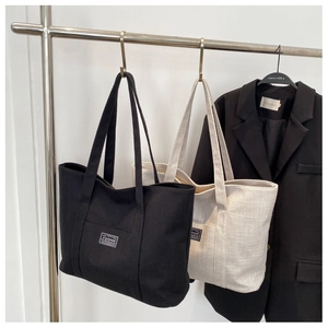 Minimalist canvas tote bag with FASHION label hanging against a black blazer background