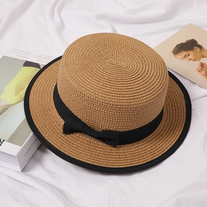 Detail of a brown woven boater hat with a black grosgrain ribbon and bow on white fabric