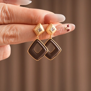 Macro detail of geometric diamond-shaped earrings in gold and dark brown resin