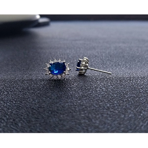 Macro detail of royal blue sapphire stud earrings with white diamond halo on gray surface