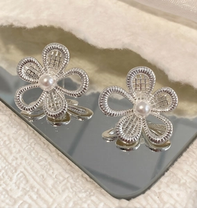 Macro shot of silver hollow flower stud earrings with central pearl on a mirror surface