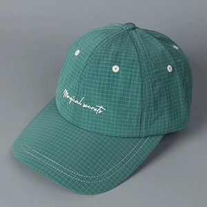 Close-up of green checkered fabric and white Magical secrets embroidery on the baseball cap