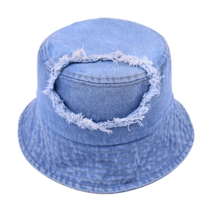 Detailed view of frayed circular hole and distressed texture on light blue denim bucket hat