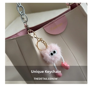 Dettaglio di un ciondolo mostro in peluche rosa con grandi occhi su una borsa