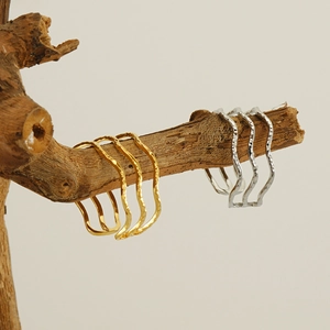 Artistic display of wavy metal bangles in gold and silver hanging on natural wood branches