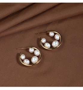 Detailed view of C-shaped gold earrings with white pearls on dark fabric background