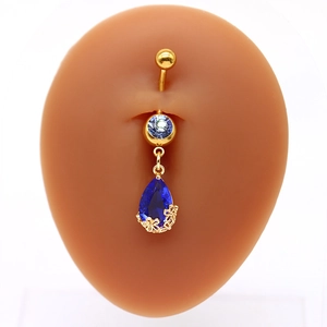 Dettaglio del piercing all'ombelico dorato con pietra blu a goccia e fiori