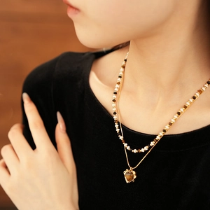 Macro shot of double-layer beaded necklace featuring a gold chain and heart tiger eye pendant