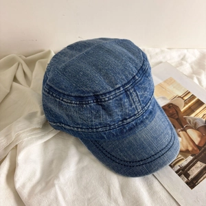 Detailed view of washed blue denim flat top hat on white fabric with fashion magazine