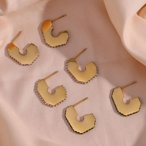 Detail of gold C-shaped earring with green gemstones on pink silk fabric background