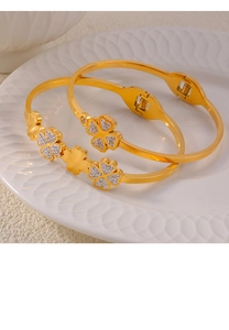 Detail of gold titanium steel bracelets with clover charms on white textured porcelain