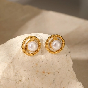 Detailed close-up of retro pearl earrings with golden twisted metal frame on white stone