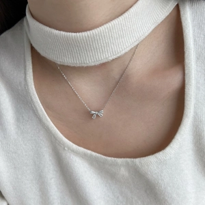 Close-up of S925 silver bow pendant necklace with shimmering cubic zirconia on white sweater