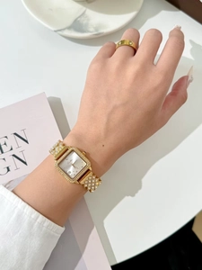 Close-up of elegant gold square watch with crystal accents and matching screw motif ring