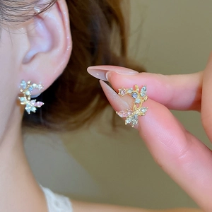 Macro detail of leaf branch earrings with pink and blue crystals on golden base