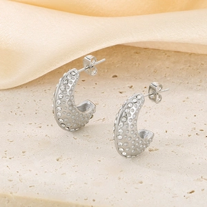 Détail macro de boucles d'oreilles C argentées avec cristaux et texture gravée