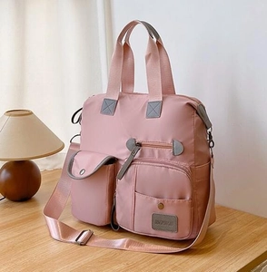 Detail of pink nylon multi-pocket tote bag showing the textured material and front zippers