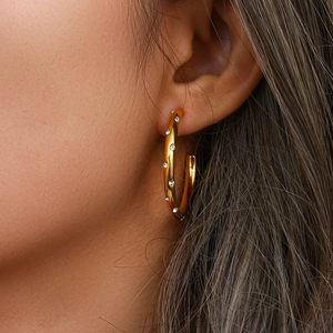 Detailed close-up of a 18K gold plated earring with small white zircon crystals on a model