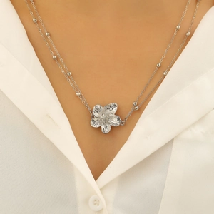 Detail van zilveren bohemian plumeria bloem met geborstelde metaaltextuur en kralenketting