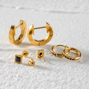 Three-piece set of gold stainless steel earrings with black rhinestones on white texture