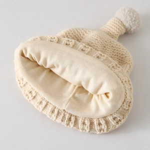 Detailed macro view of beige knitted baby hat showing soft lining and fluffy pompom