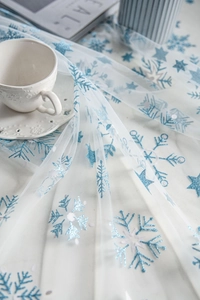 Detailed view of white mesh fabric with blue sequin snowflakes and star embroidery