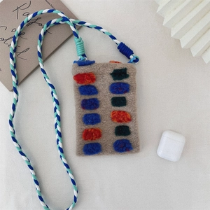 Detail of plush khaki pouch with colorful pom-poms and braided strap for AirPods