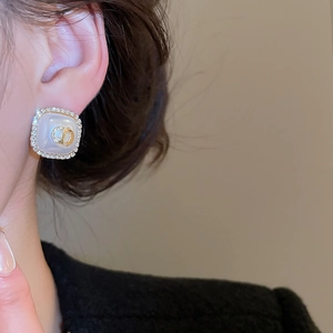 Close-up of square pearl earrings with golden CD logo and diamond-encrusted border