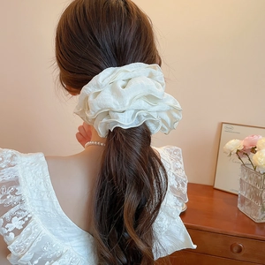 Detail of a large white pleated chiffon scrunchie showing wavy ruffles on a ponytail