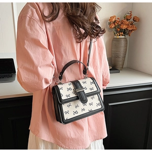 Piccola borsa a mano quadrata alla moda con motivi a fiocco nero indossata da una modella