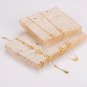 Golden beaded anklet with traditional copper coin charms displayed on a stone pedestal