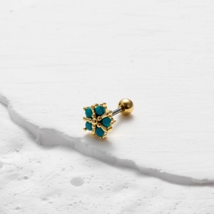 Macro shot of gold flower stud earring with turquoise stone on white stone background